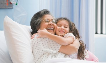 Abuela en cama de hospital abrazando a su nieta