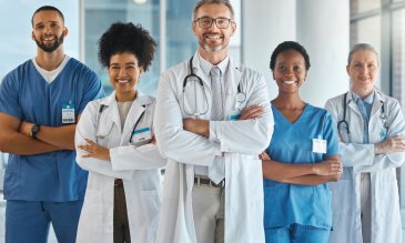Fotografía de Stock de cinco profesionales médicos de pie en una fila con los brazos cruzados y sonriendo