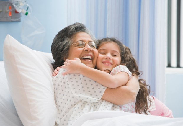 Grandmother in hospital bed hugging her granddaughter