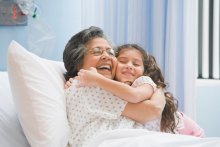 Grandmother in hospital bed hugging her granddaughter