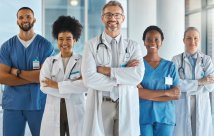 Fotografía de Stock de cinco profesionales médicos de pie en una fila con los brazos cruzados y sonriendo